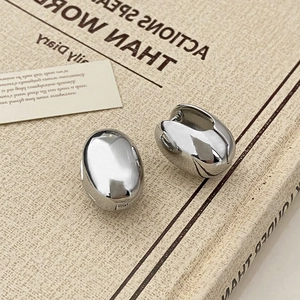 Detailed view of polished silver oval hoop earrings with a mirror-like finish on a book