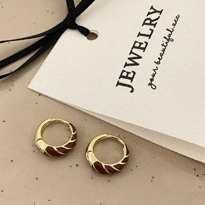 Macro shot of gold-plated spiral twist earrings with brown enamel on a textured card