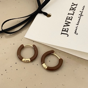 Detailed shot of gold and brown enamel huggie earrings on a stylish jewelry card