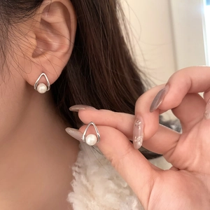 Macro detail of teardrop-shaped silver earrings featuring a round white pearl on ear