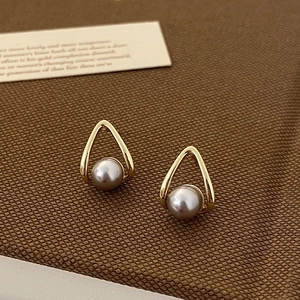 Detailed shot of golden triangular pearl earrings on brown fabric with a decorative card