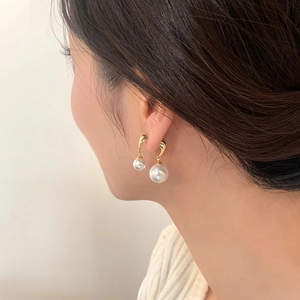Elegant gold drop earrings with lustrous white pearls worn by a model in a side profile