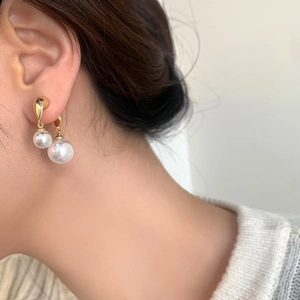 Close-up of elegant gold drop earrings with lustrous white pearls on female model