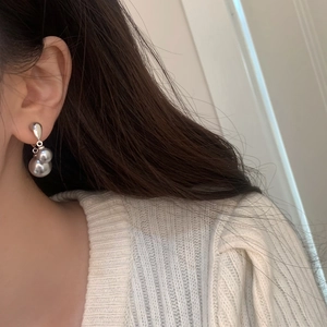 Close-up of minimalist silver double pearl drop earrings worn by a model in a white sweater