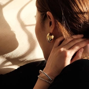 Close-up of a gold chunky hoop earring and twisted rope bangle worn by a model in soft light