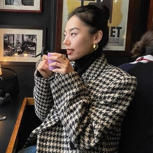 Elegant woman wearing large gold eggshell hoop earrings and houndstooth blazer in a cafe