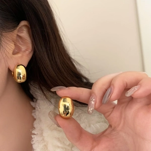 Close-up of high-polish golden egg-shaped stud earrings showing a smooth metallic finish