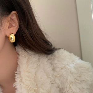 Close-up of a polished gold oval earring on a model wearing a soft white coat