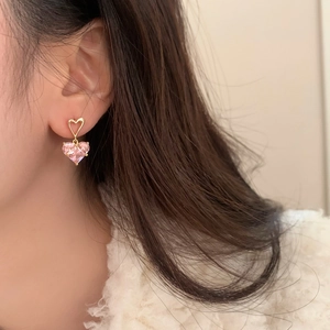 Détail de boucles d'oreilles cœur en cristal rose portées avec un pull en maille crème