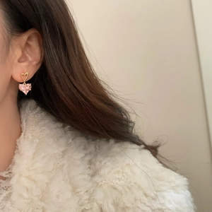 Détail d'une boucle d'oreille cœur rose et perle dorée portée sur un modèle avec douceur