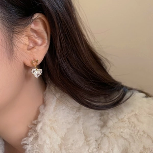 Vue détaillée d'une boucle d'oreille cœur en cristal avec finition dorée sur modèle