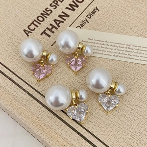Détail de boucles d'oreilles perles et pierres roses en cœur avec monture dorée