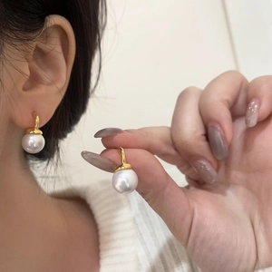 Detail view of large white pearl earrings with elegant gold hooks on female model