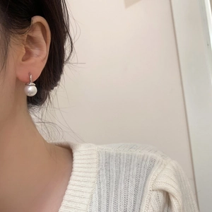 Detailed view of an elegant white pearl drop earring with a silver hook on a model