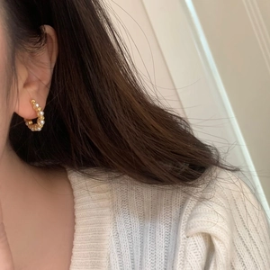 Detail of C-shaped gold pearl hoop earrings worn by a model in a knit sweater