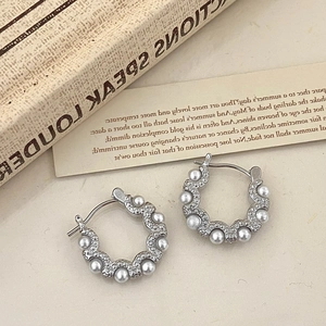 Close-up of wavy silver hoop earrings with tiny zircons and pearls on vintage book