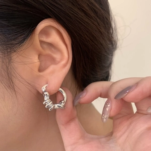 Dettaglio di orecchini a cerchio intrecciati in argento indossati per uno stile minimalista