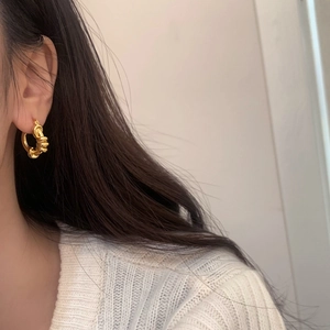 Dettaglio di orecchini a cerchio dorati a spirale su modella in stile minimalista