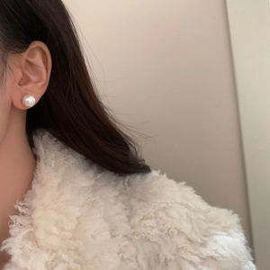 Detailed close-up of large round white pearl earring worn by model in soft lighting