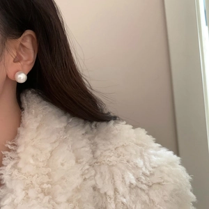Elegant classic white pearl stud earring shown on a model wearing a soft white coat