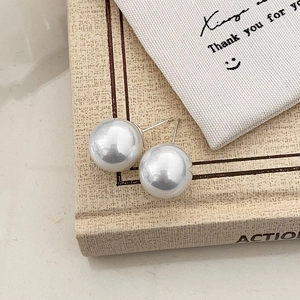 Close-up of large pearl stud earrings with metallic posts on vintage book background