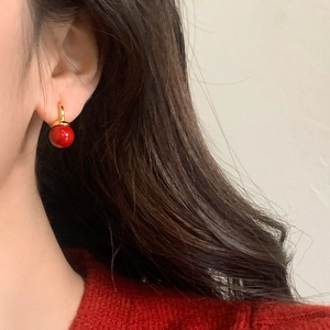 Detail von eleganten roten Perlenohrringen mit Goldhaken, getragen zu einem roten Pulli