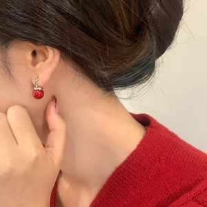 Nahaufnahme eleganter roter Perlenohrring an Model in einem roten Strickpullover