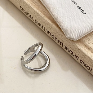 Detail of silver dual-layer crossover ring with high-polish finish on a beige background