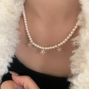 Collier de perles élégant avec trois pendentifs fleurs en zircon doré sur un manteau