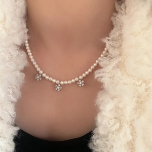 Collier de perles élégant avec trois fleurs en zircon porté sur un manteau blanc