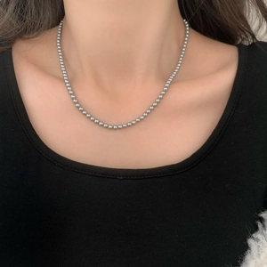 Détail d'un collier de perles gris foncé porté sur un pull en maille noire pour femme
