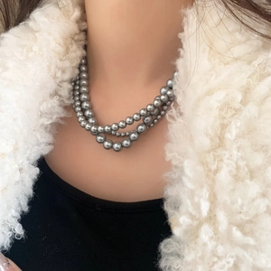 Détail d'un collier de perles grises à trois rangs avec éclat métallique sur un pull noir