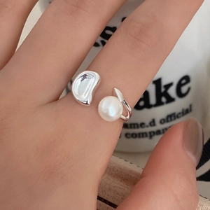 Detail of minimalist silver open ring with white pearl and organic bean element on finger