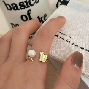 Detail view of a minimalist gold open ring with a round white pearl and organic metal plate