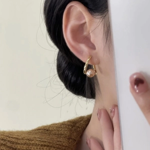 Détail de boucles d'oreilles perles dorées en U portées, style élégant et minimaliste