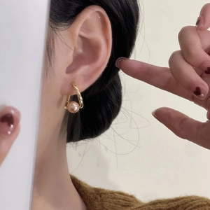 Gros plan sur une boucle d'oreille créole dorée avec perle rose portée par un mannequin