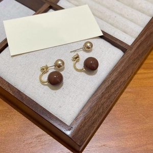 Dettaglio orecchini a doppia perla marrone vintage con finiture dorate su tessuto bianco