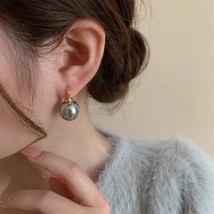 Close-up of a grey pearl earring with gold clasp worn by a model in a mohair sweater