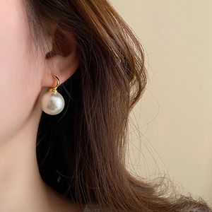 Detailed close-up of a large white round pearl earring with an elegant gold hook fastener