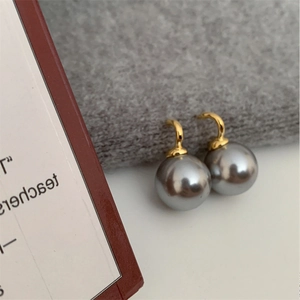 Detail of silver gray pearl earrings with gold hooks against a soft knit background