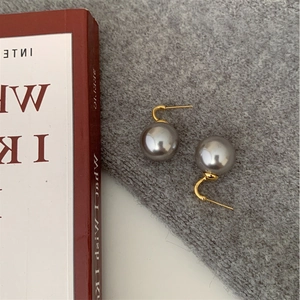 Close-up of elegant grey pearl earrings with gold hooks on a soft grey knit fabric