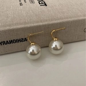Detail shot of round white pearl earrings with minimalist gold curved hooks on a book