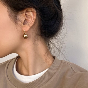 Elegant gold spherical stud earrings with polished mirror finish on model ear side view