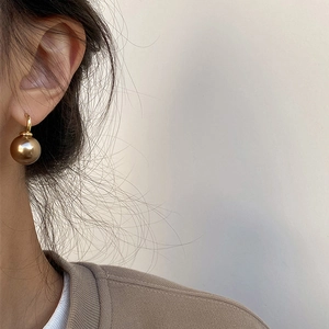 Close-up of model wearing gold spherical pearl drop earrings with minimalist metal finish