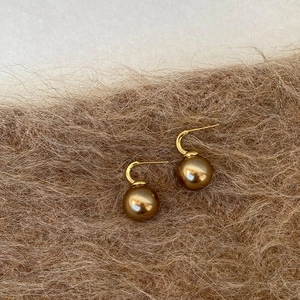 Detail view of coffee gold pearl drop earrings on soft brown fabric texture background
