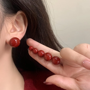 Elegant deep red pearl stud earrings in various sizes shown on a model and hand