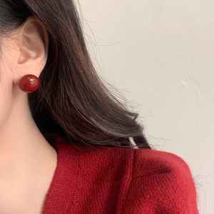 Elegant glossy dark red round pearl stud earrings worn by a model in a red sweater