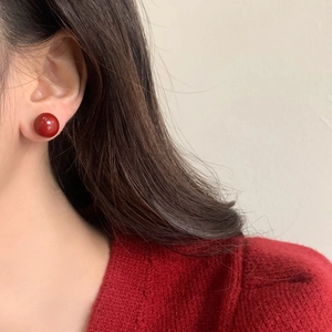 Close-up of elegant red spherical pearl stud earring worn with a matching red knit sweater