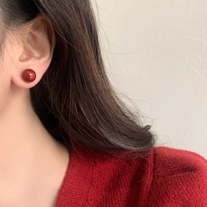 Close-up of a vintage deep red round stud earring worn with a cozy red knit sweater