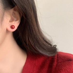 Close-up of vibrant red spherical stud earrings worn by a model in a red sweater